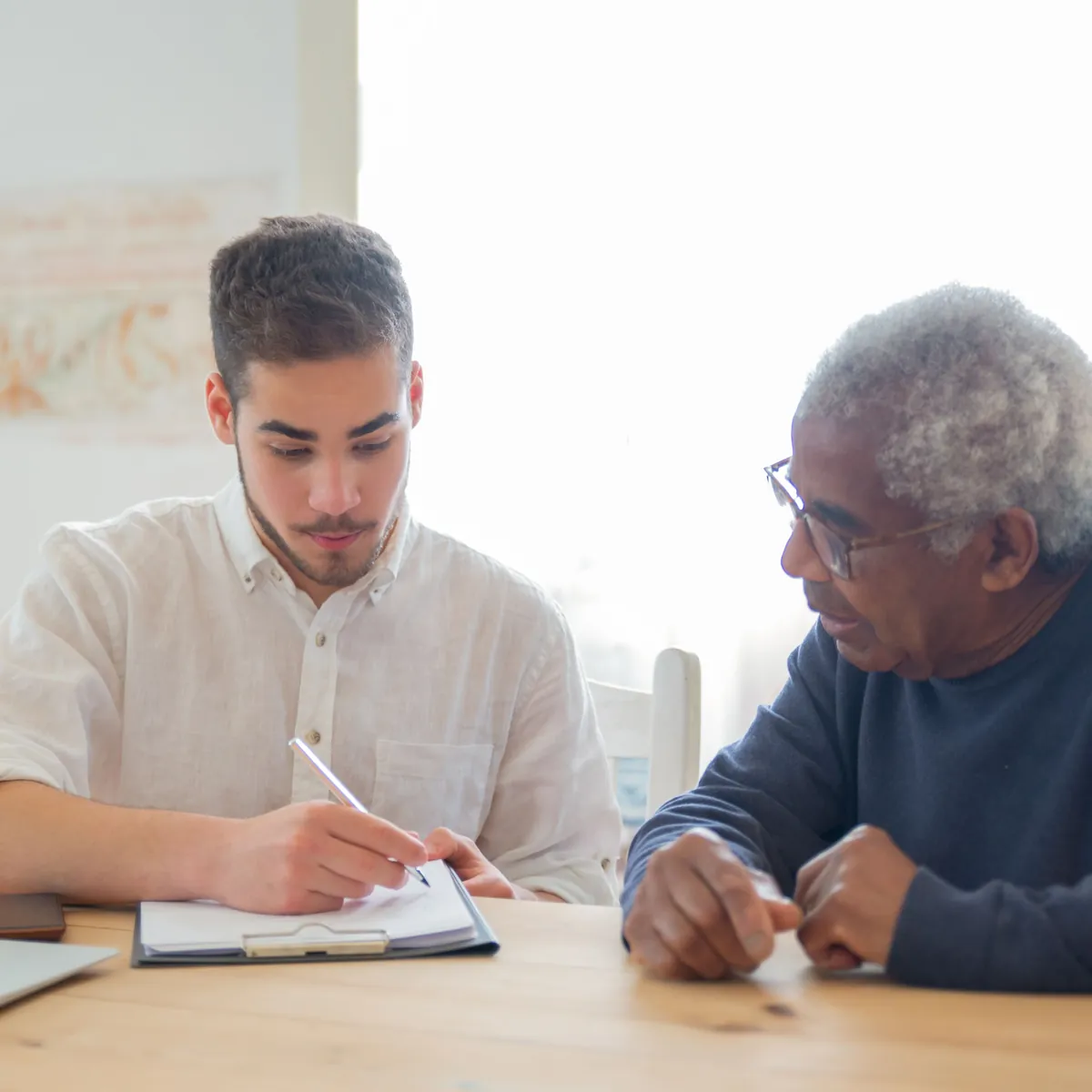 A support worker writing up a plan with an older man at his dining table