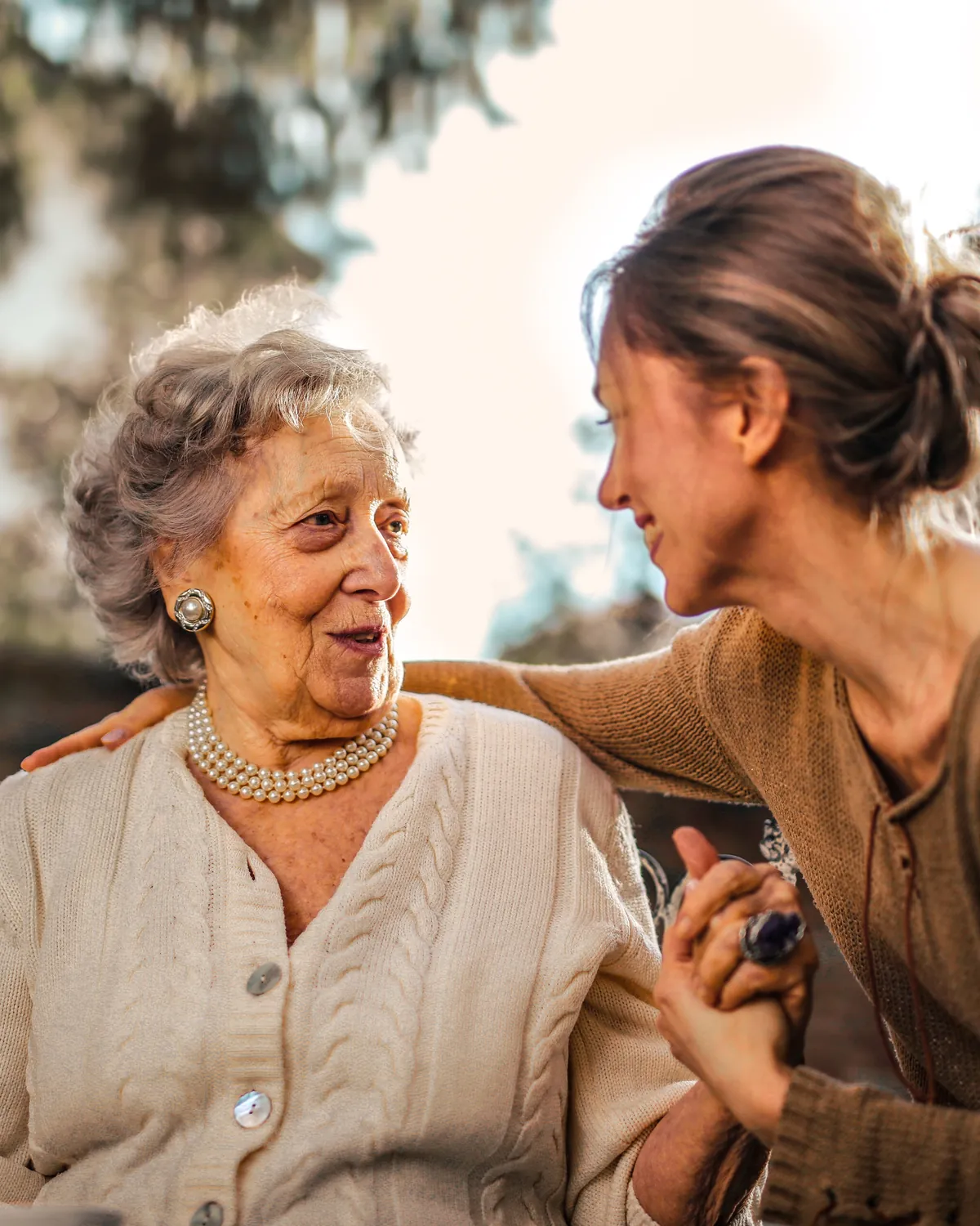 A smiling woman with her arm around her elderly mother, holding her hand