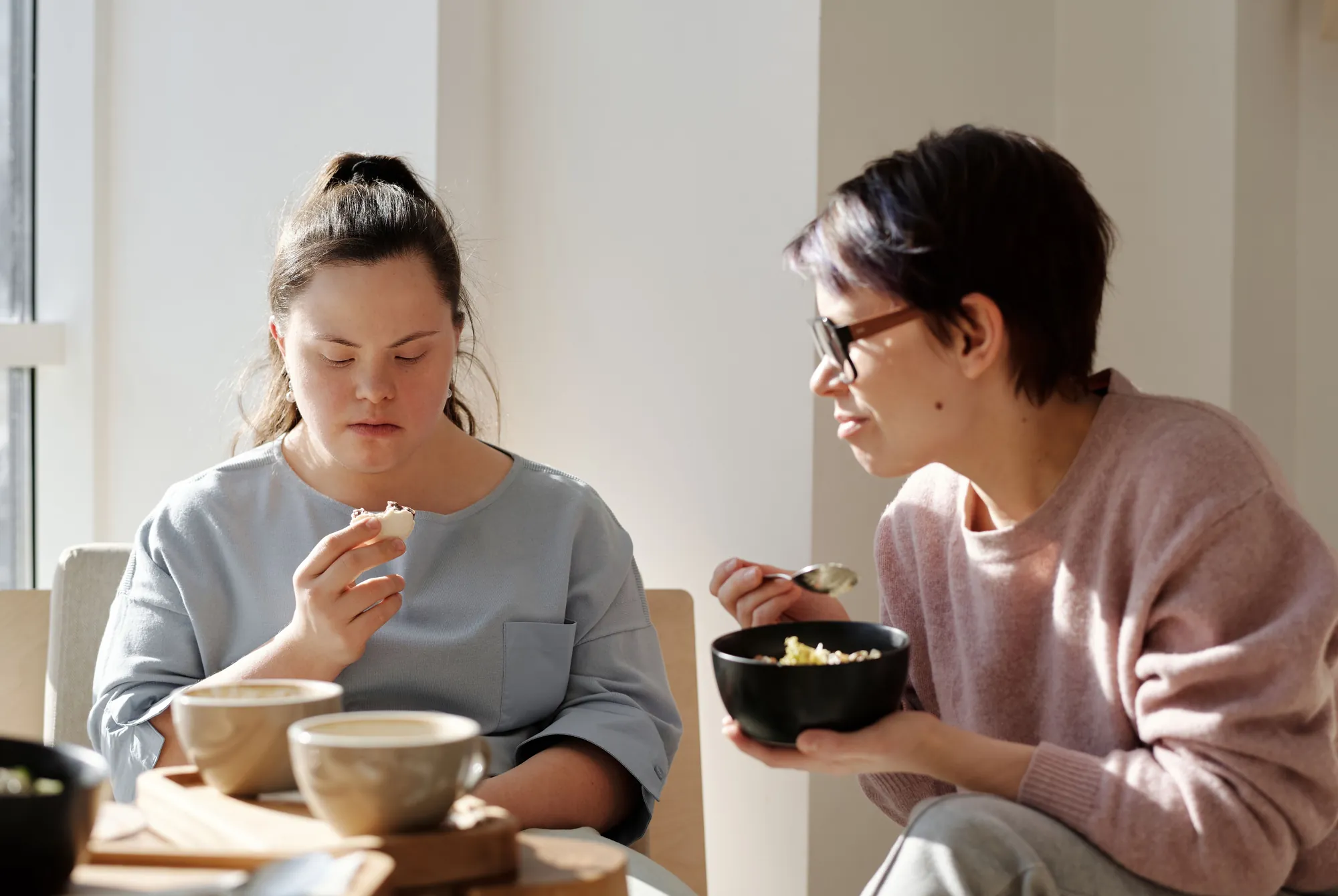 A young woman with Down's syndrome having breakfast with a support worker at her kitchen table