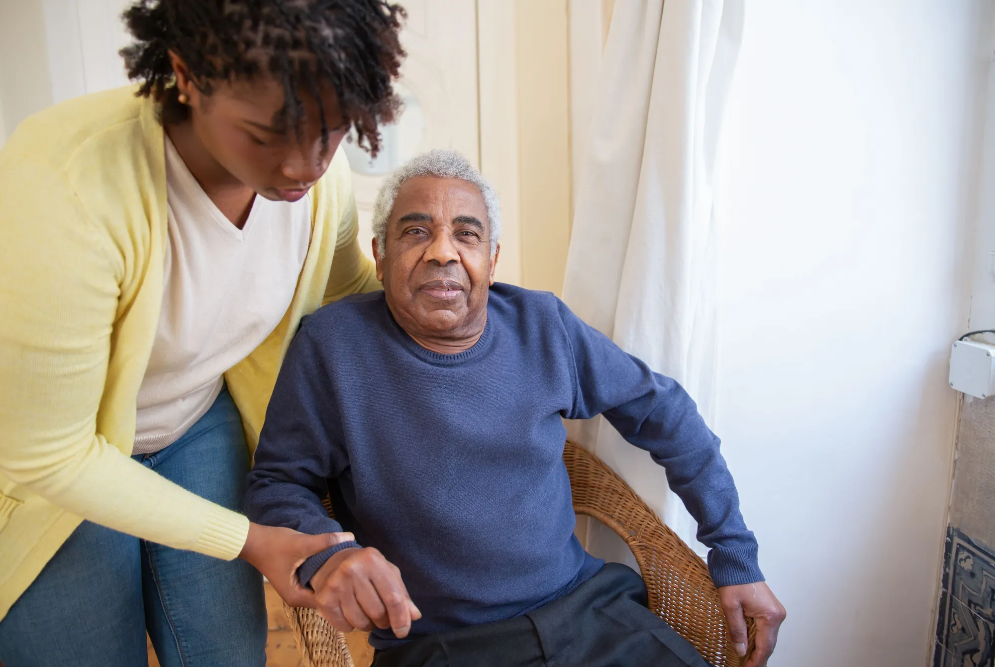 A support worker helping an older man up from his armchair